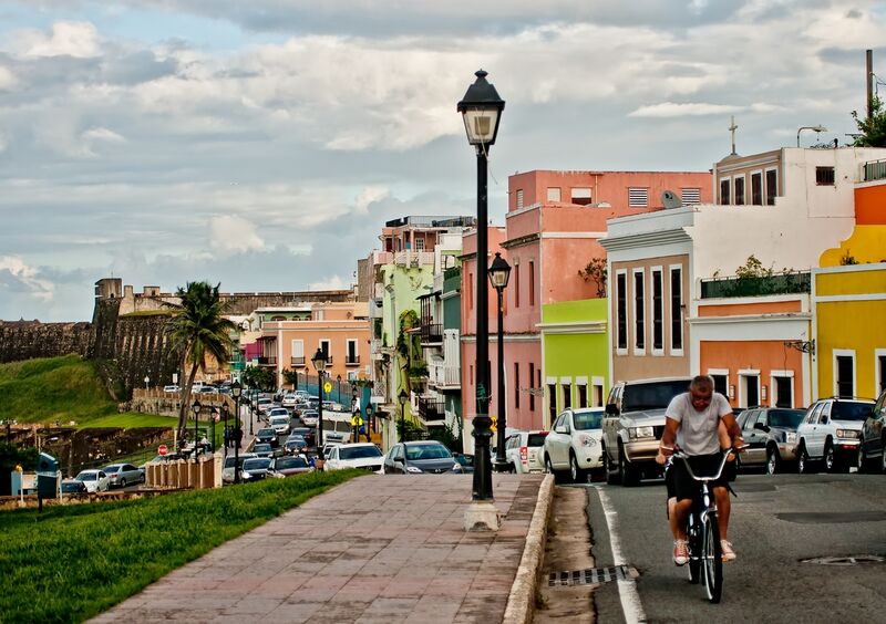 Cars, houses, street light, man on bicycle and El Morro in Old San Juan
